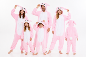 Kinderen en volwassenen in zachte roze konijn onesies met lange oren, witte buik en pluizige konijnenstaart.